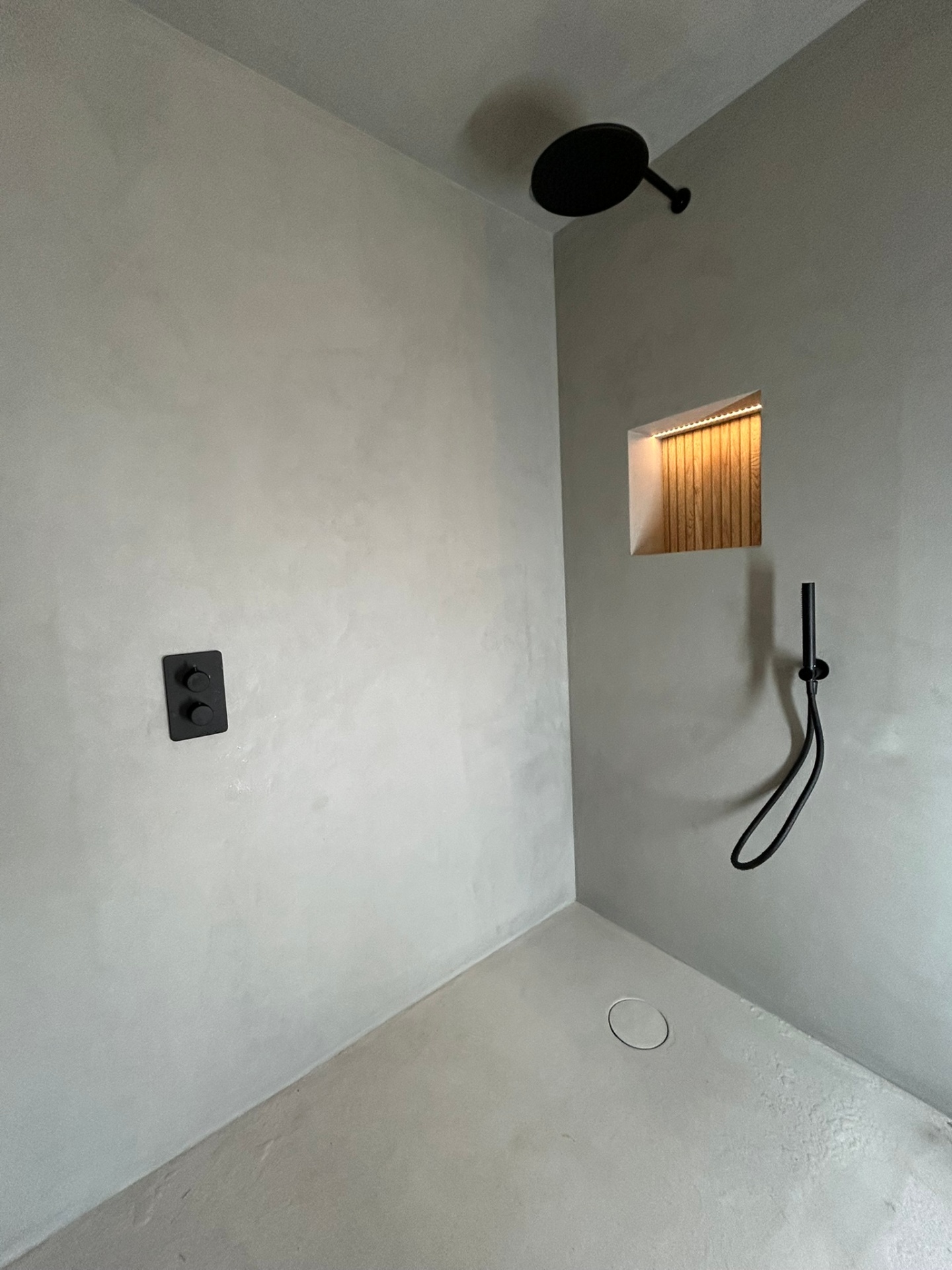 Microcement walk-in shower with black rainfall head and niche