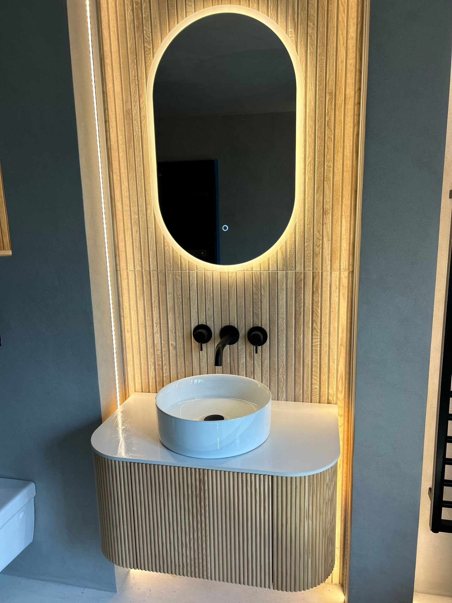 Microcement bathroom with fluted vanity and backlit oval mirror