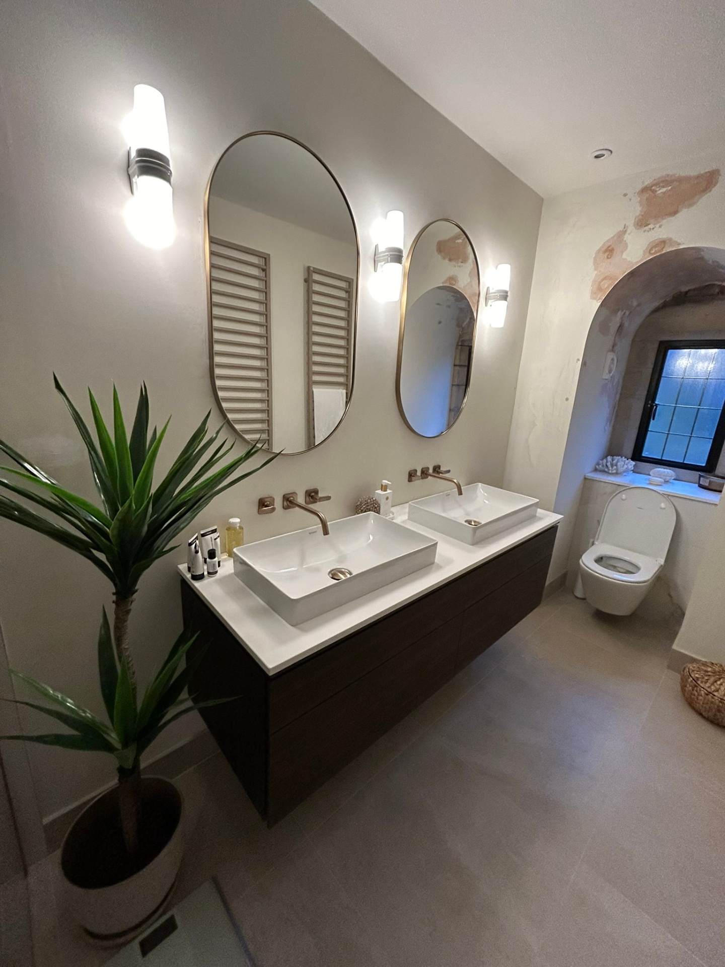 Double vanity with arched mirrors and warm wall lights